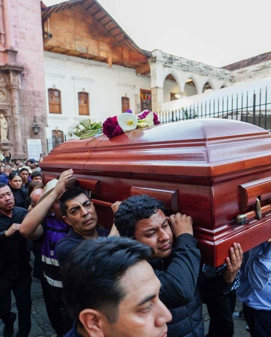 Varias personas cargan un ataúd afuera de una iglesia.